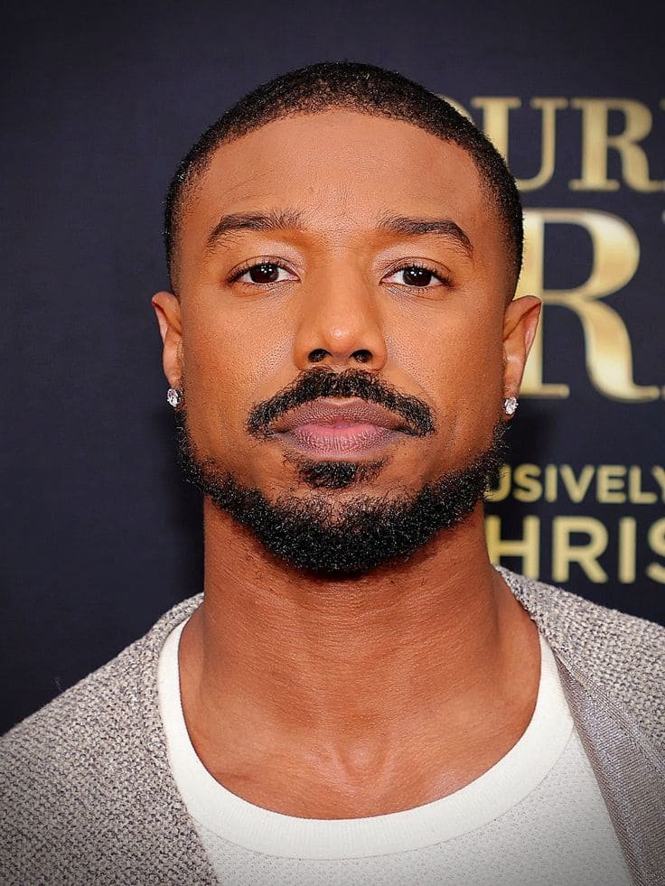 Full Beard with Taper Fade Michael B. Jordan with a full beard and clean taper fade, wearing a textured jacket over a white shirt
