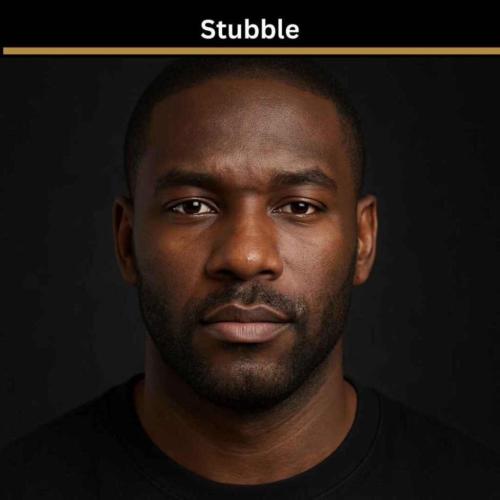 Black man with a low haircut and neatly shaped stubble beard against a dark background. Example of a professional stubble style for patchy beard coverage.” Black man with a low haircut and neatly shaped stubble beard against a dark background. Example of a professional stubble style for patchy beard coverage.”