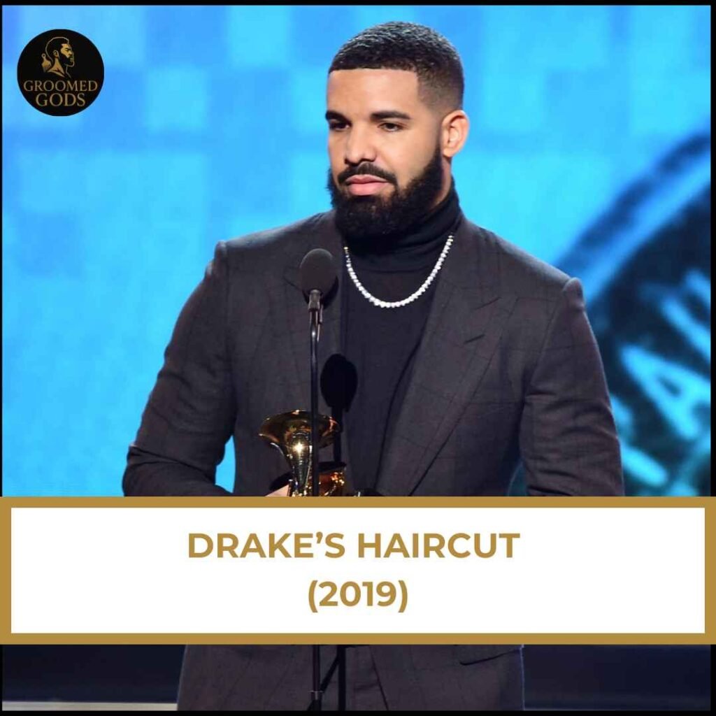 Drake’s Haircut (2019) Drake with a high fade and waves hairstyle in 2019 while wearing a suit on stage at an award show.